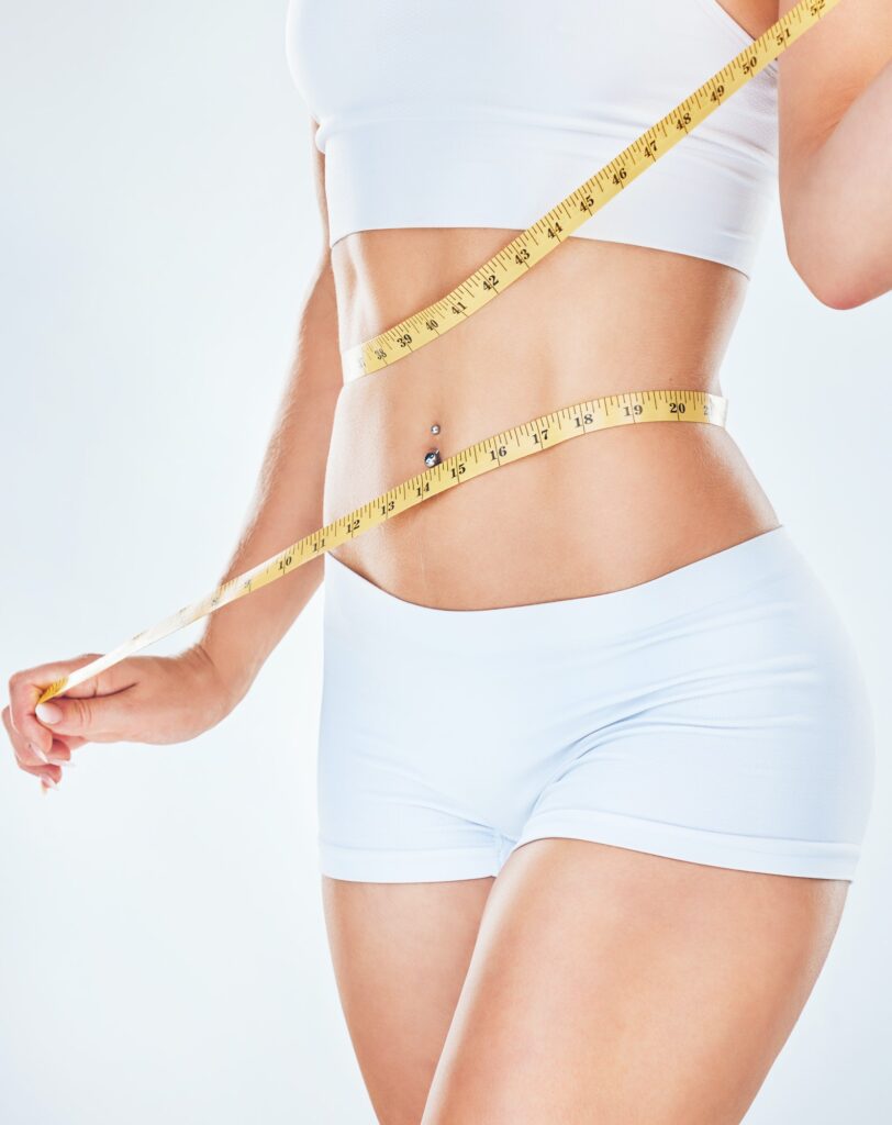 Body, tape measure and diet with a woman measuring her waist to track weightloss in studio on a gra